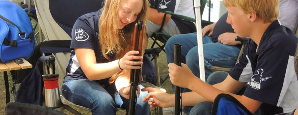 Young people assembling air rifles outdoors.